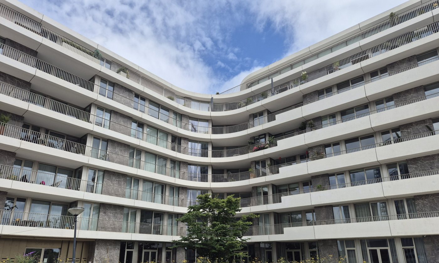 Curved white apartment building with continuous balconies and full-height uPVC windows