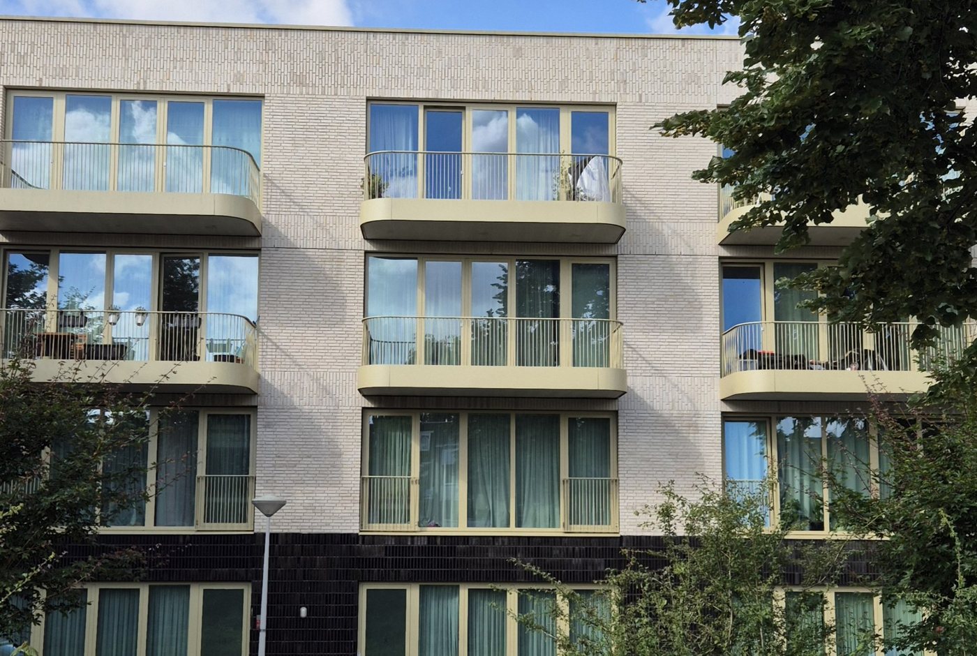 Pale brick apartment building with rounded balconies and bronze-coloured uPVC windows