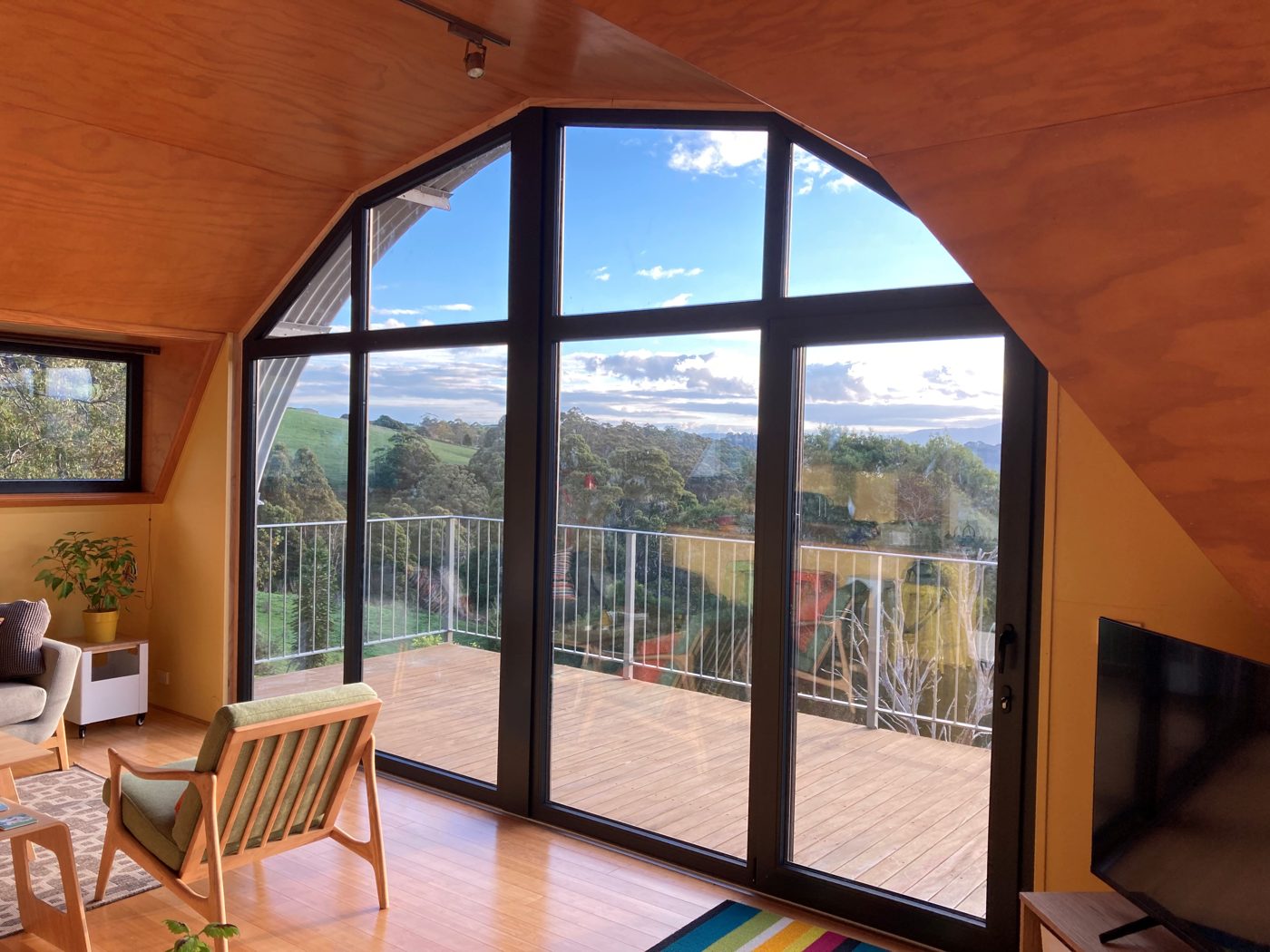Arched uPVC window wall with a sliding door, seen from inside looking out to a deck and hills