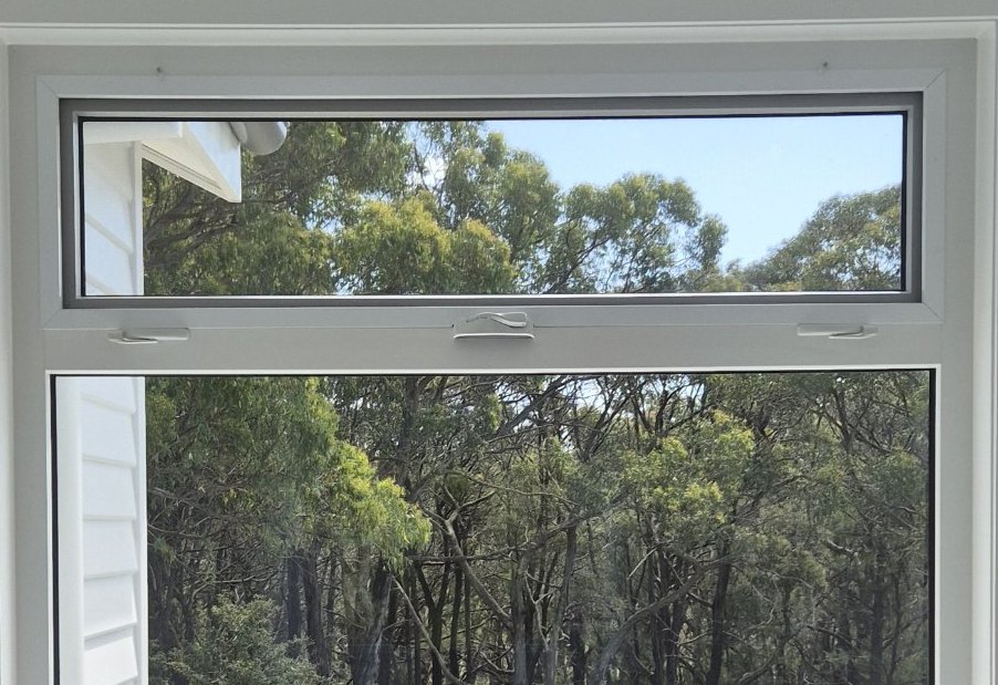 White uPVC awning sash with winders above a large fixed window, looking out to gum trees