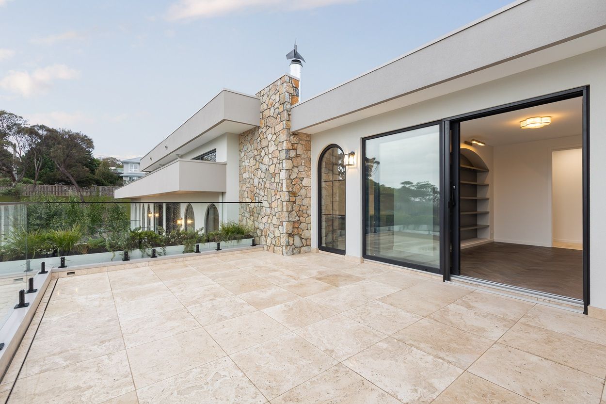 Terrace with a stone chimney, a black-framed arched window and a wide black sliding door opening to the lounge