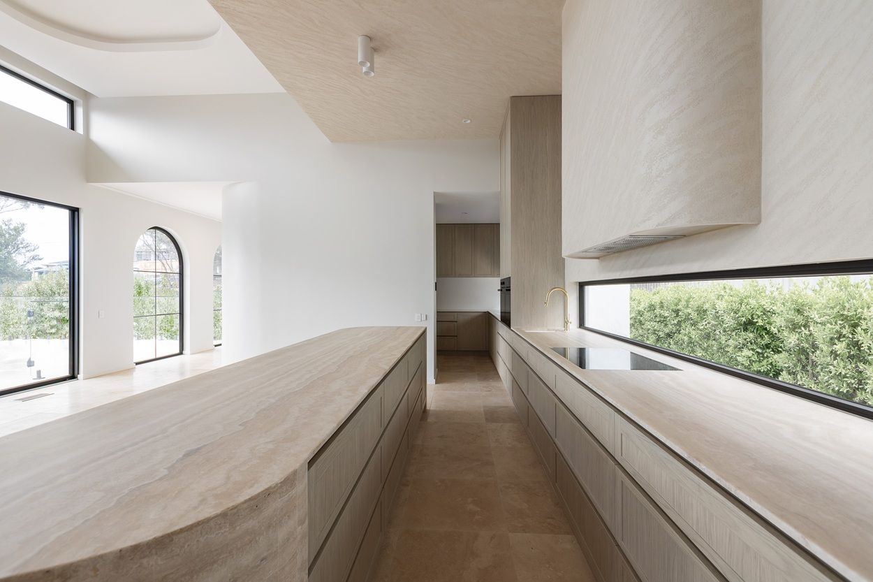Kitchen with a long travertine island, a strip window above the bench and black-framed arched windows beyond