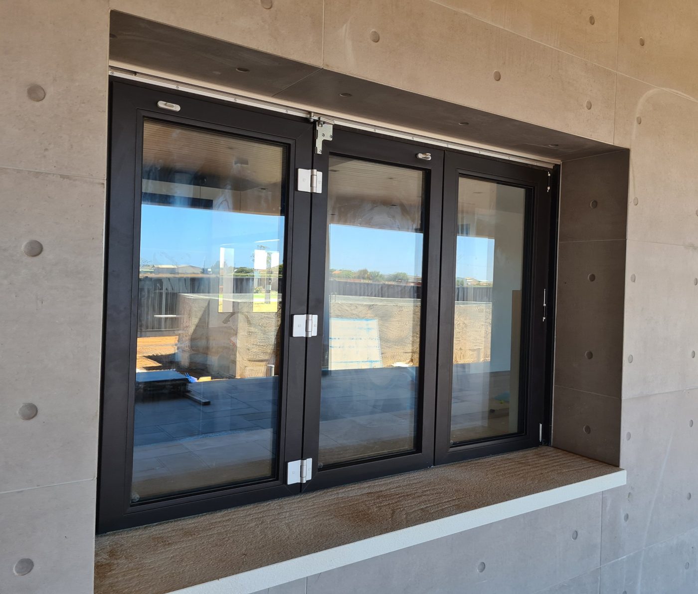 Three-panel charcoal uPVC bifold window set into a rendered wall above an outdoor benchtop