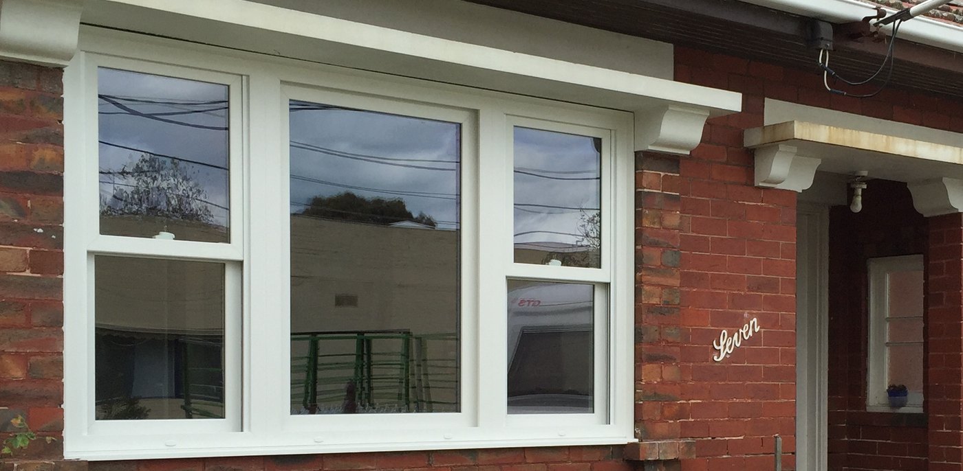 White uPVC double hung windows either side of a fixed centre pane, fitted to a red-brick period home