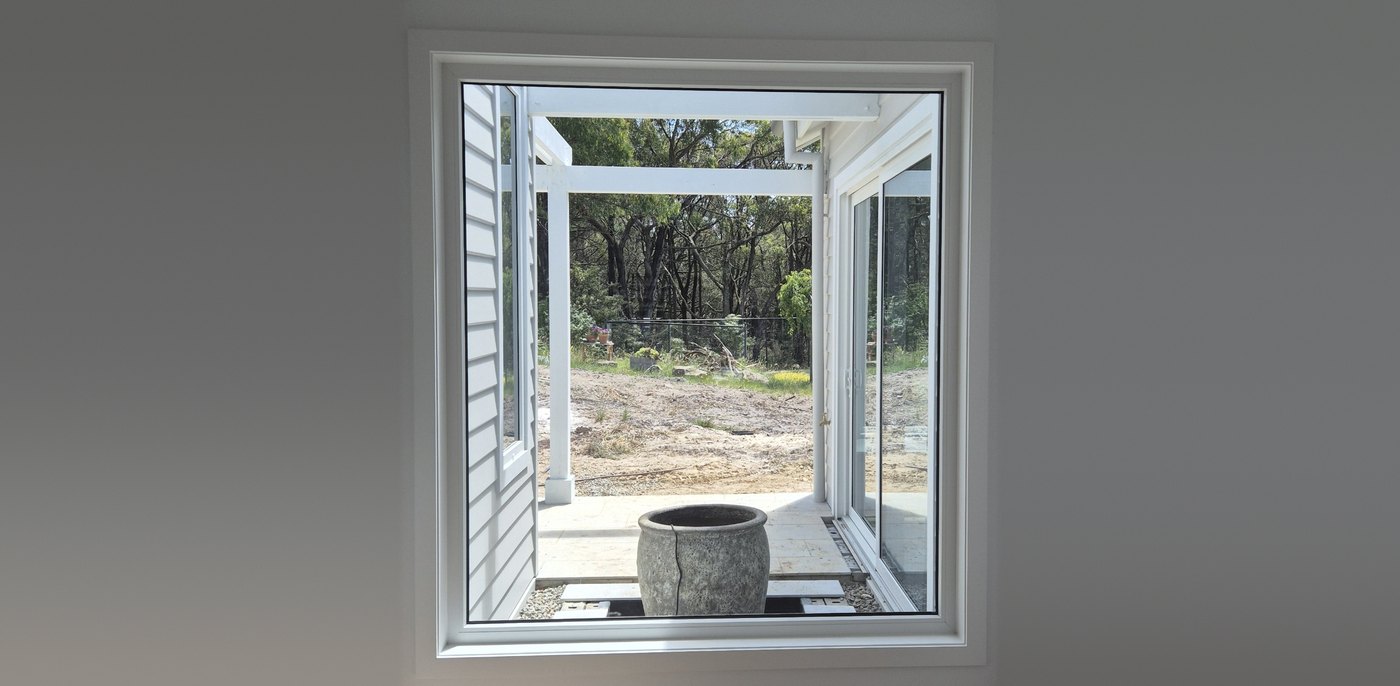 Large white uPVC fixed window in a hallway, framing a courtyard, verandah and bushland