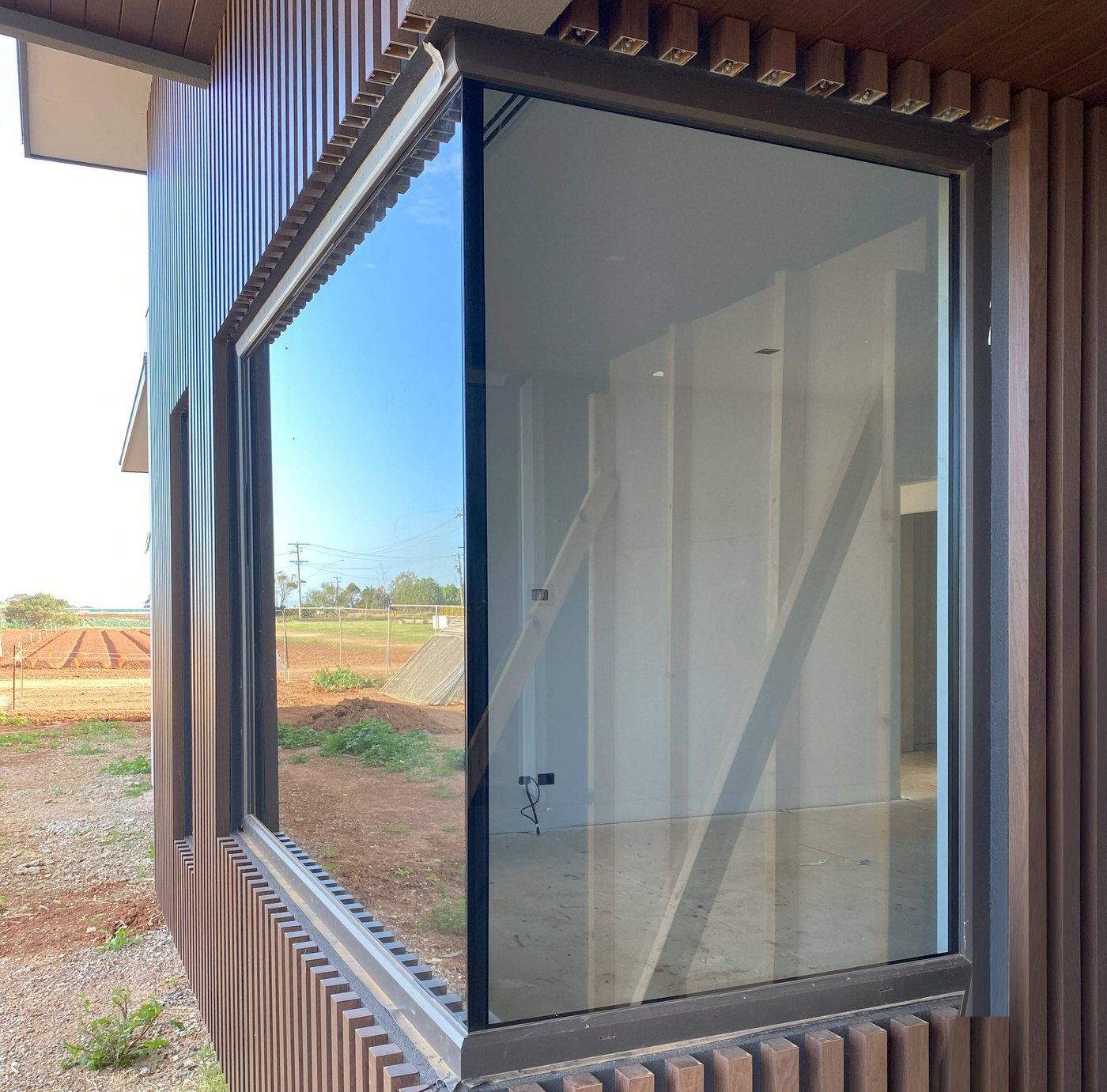 Dark-framed corner window where two panes of glass meet at the corner without a post, set in timber-look cladding