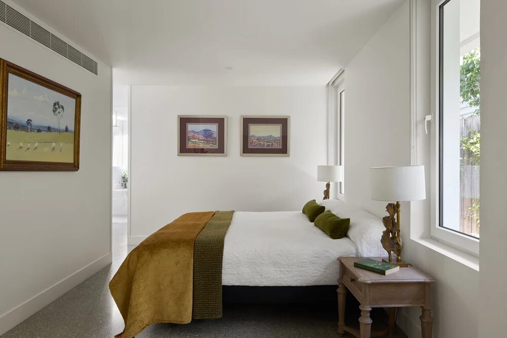 Bedroom lit by tall white-framed windows beside the bed