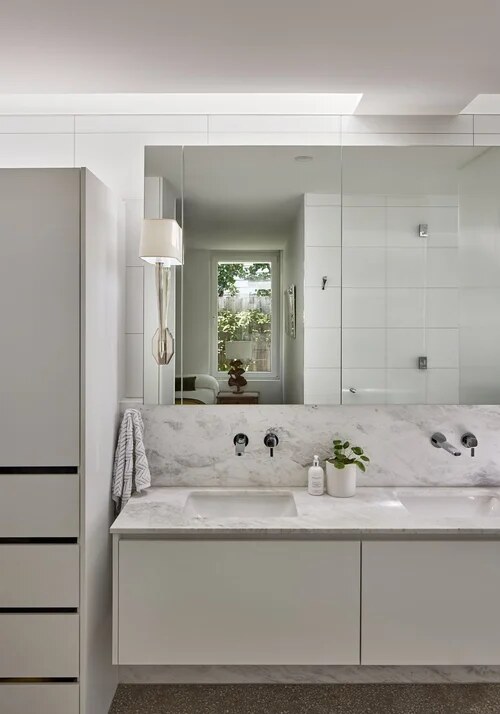 White bathroom vanity with a marble benchtop, its mirror reflecting a white-framed window