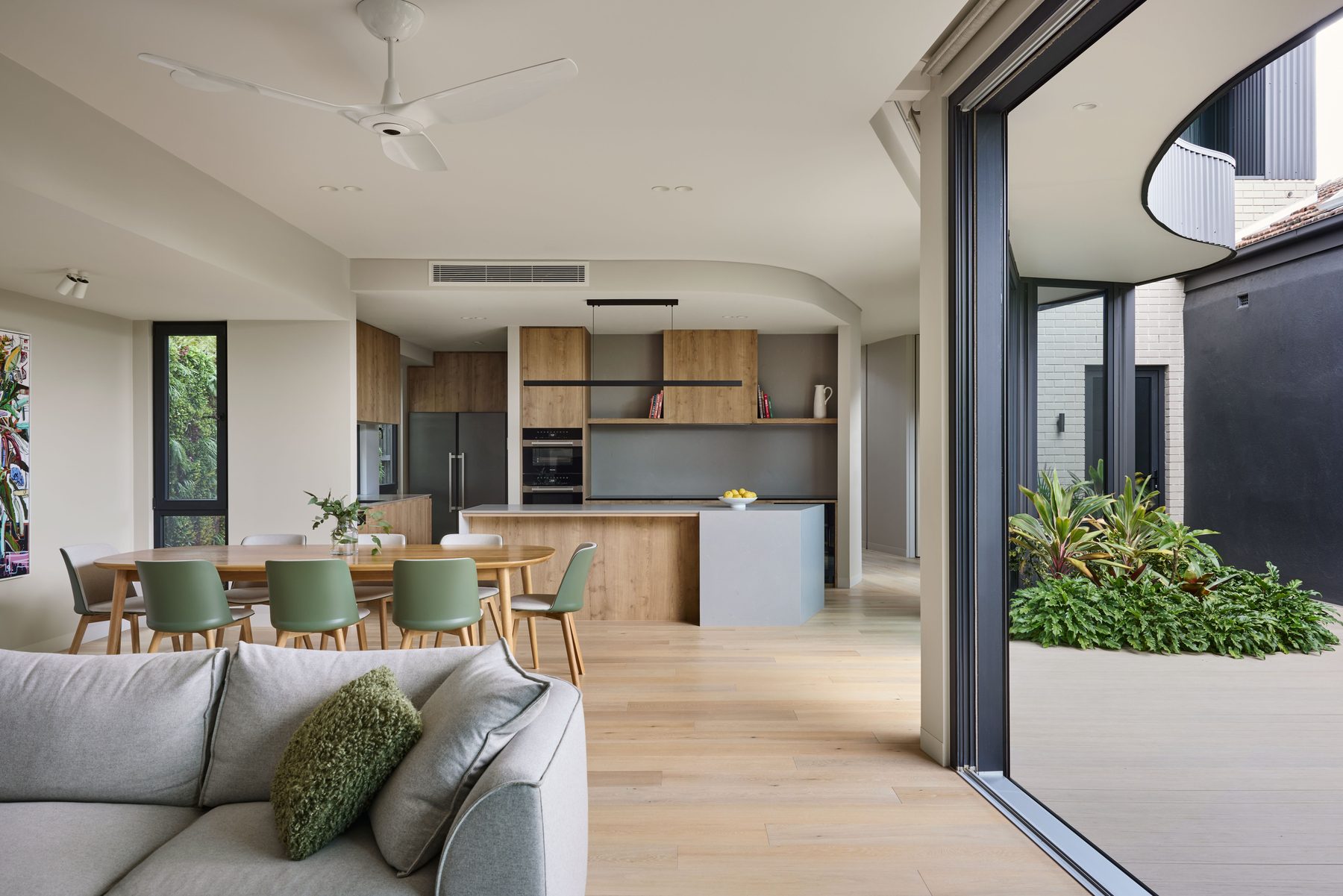 Open-plan living, dining and kitchen opening through a wide charcoal uPVC sliding door to a planted courtyard