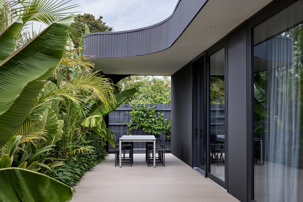 Covered deck with charcoal uPVC doors beneath a curved corrugated eave