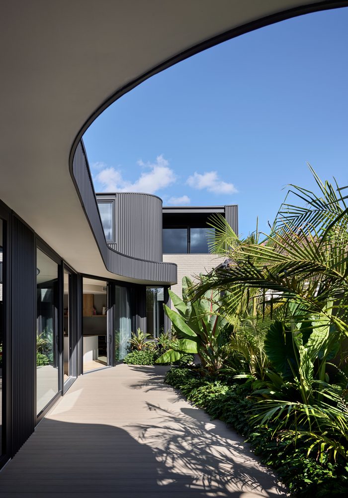 Courtyard walkway lined with floor-to-ceiling charcoal uPVC glazing under a sweeping curved roof