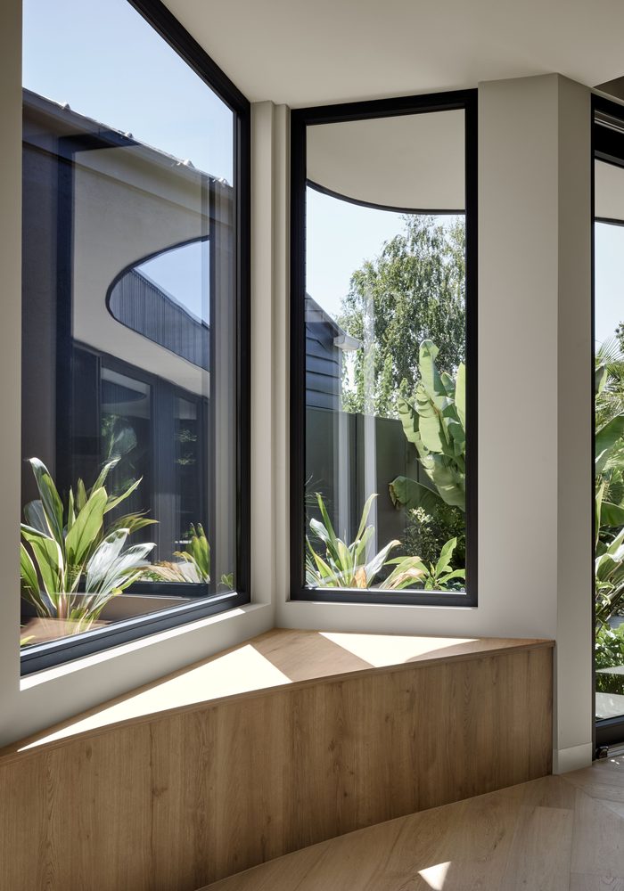 Corner window seat framed by black uPVC windows looking out to tropical planting