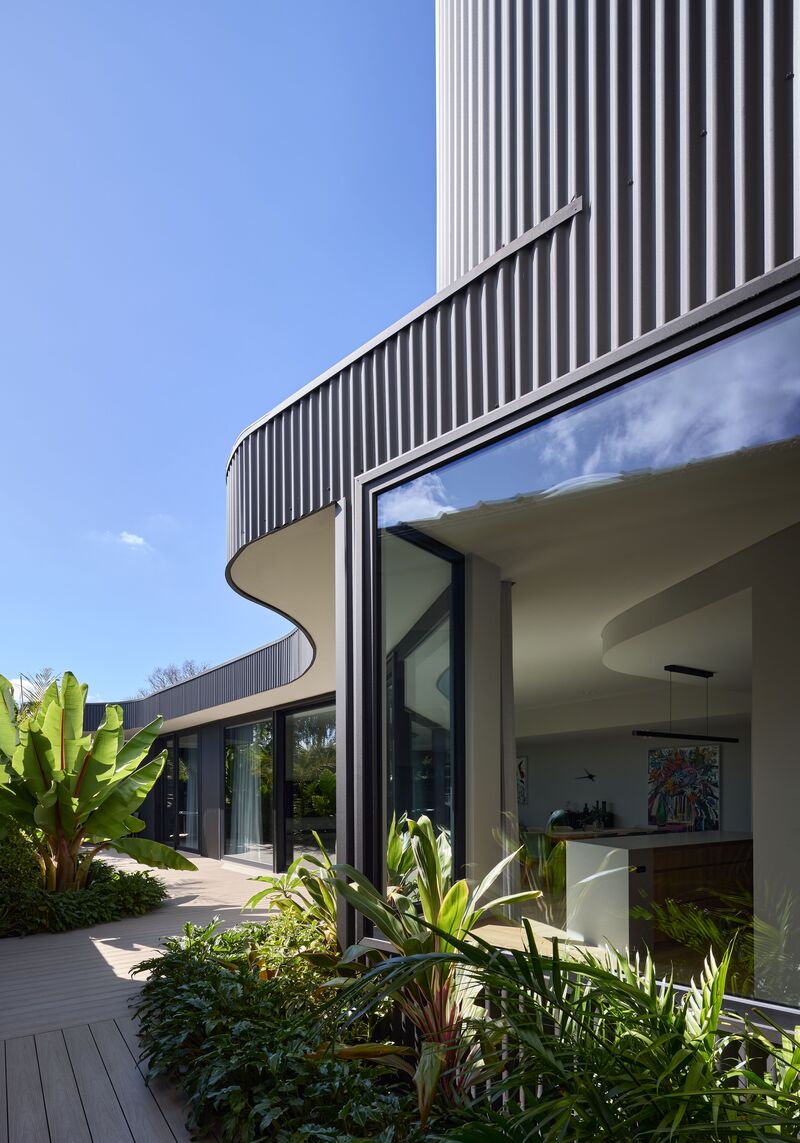 Large black-framed corner window under a curved corrugated eave, looking into the kitchen and dining room
