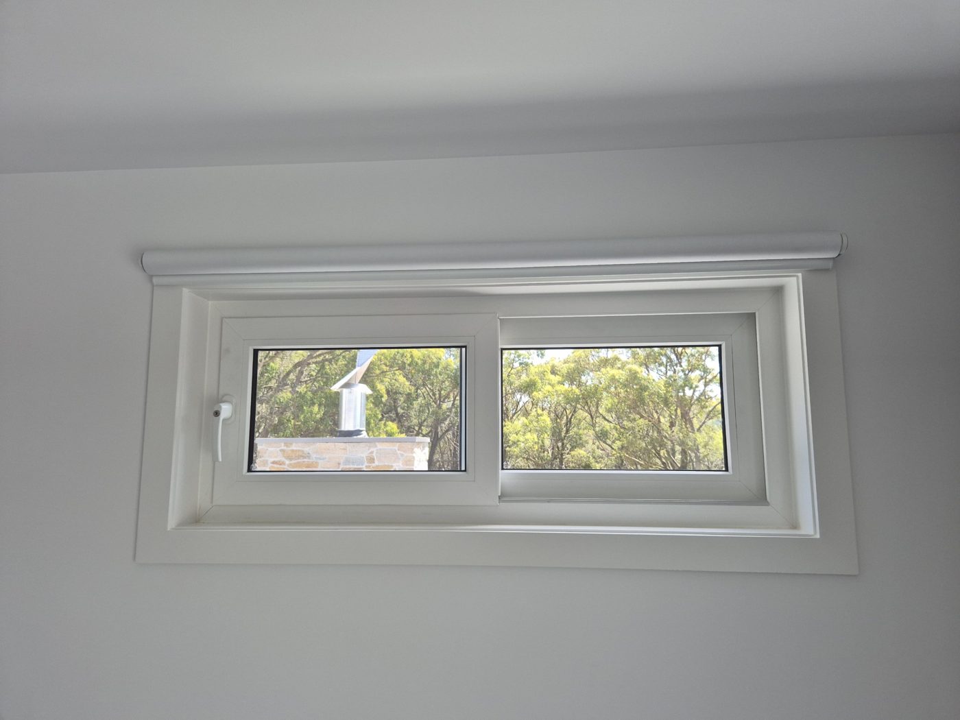 White uPVC sliding window with two sashes set high in a bedroom wall, looking out to gum trees
