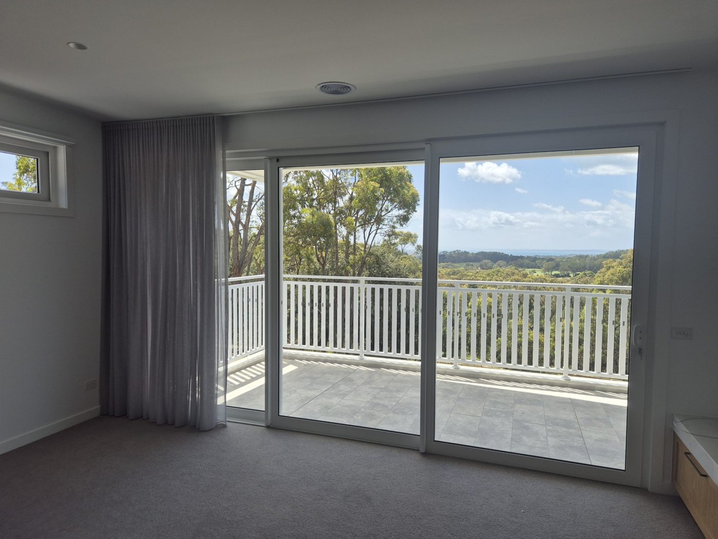 White uPVC stacking door with three panels opening onto a balcony with bushland and sea views