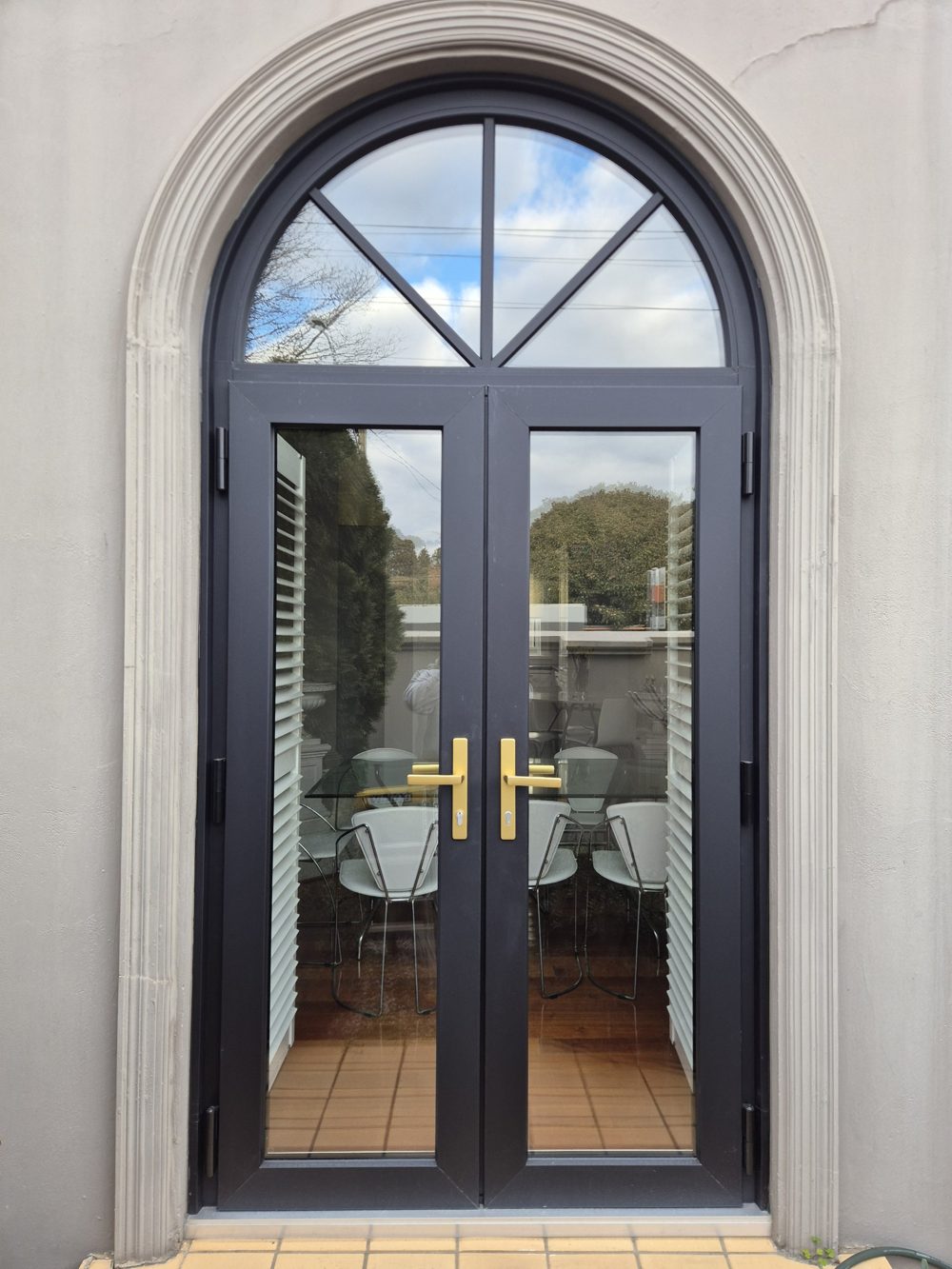 Charcoal uPVC French doors with an arched fanlight above, set into a rendered arch with brass handles