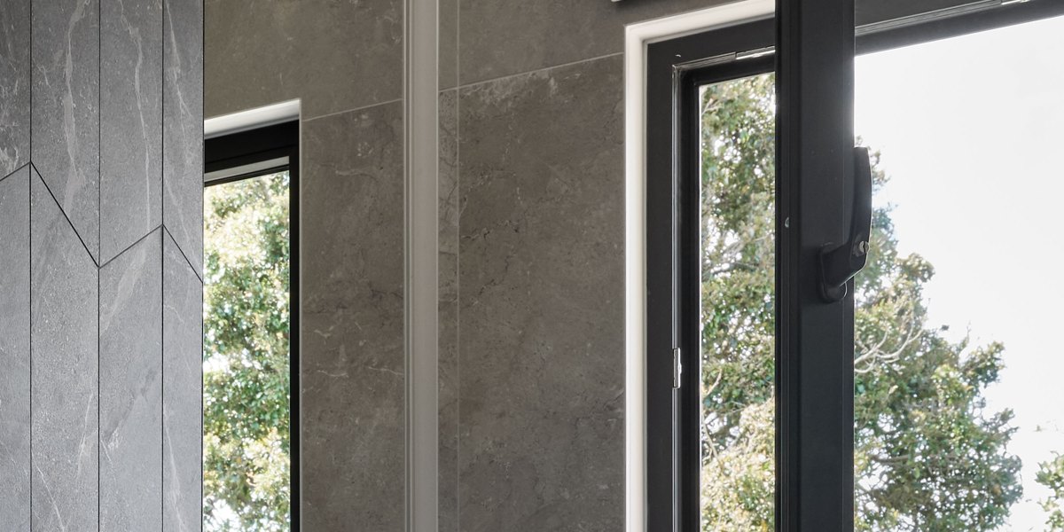 Black uPVC tilt and turn window with its sash turned inward, beside a stone-look tiled bathroom wall