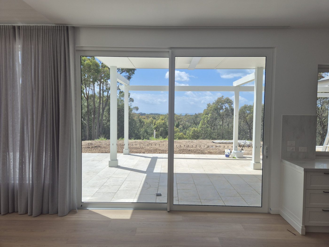 White uPVC Vario Slide door from a living room out to a covered patio and gum trees